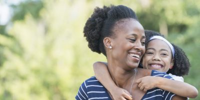 Portrait of an African American mother with her beautiful mixed race young daughter. The little girl is 7 years old, part Black, Asian, Hispanic and Pacific Islander ethnicity. The woman is holding the child piggyback, looking over her shoulder.